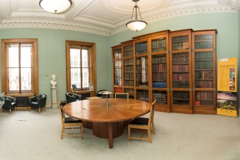 lyell room with glass cabinet bookshelves, two sahs widnows and a huge round wooden table with chairs